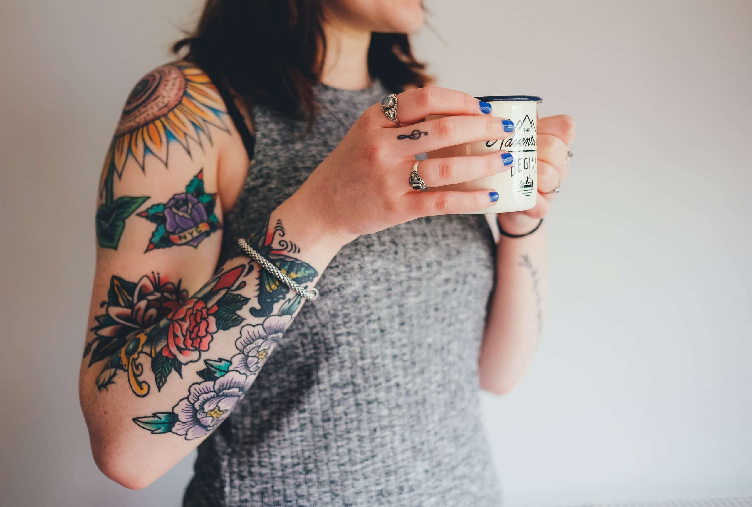 Tatuagem feminina nos braços da mulher segurando uma caneca