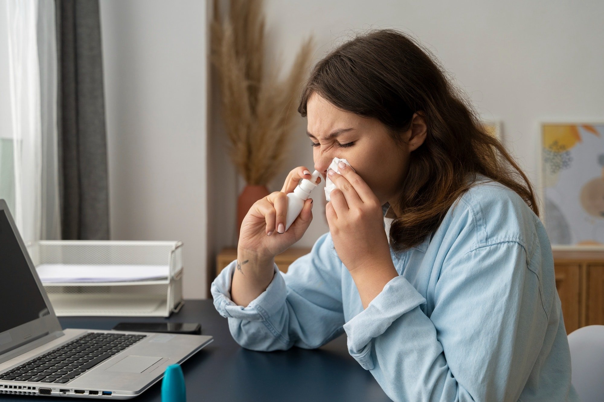 Mulher espirrando, segurando spray nasal.