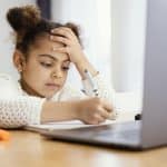 Menina estudando de frente para notebook, aparentando preocupação.