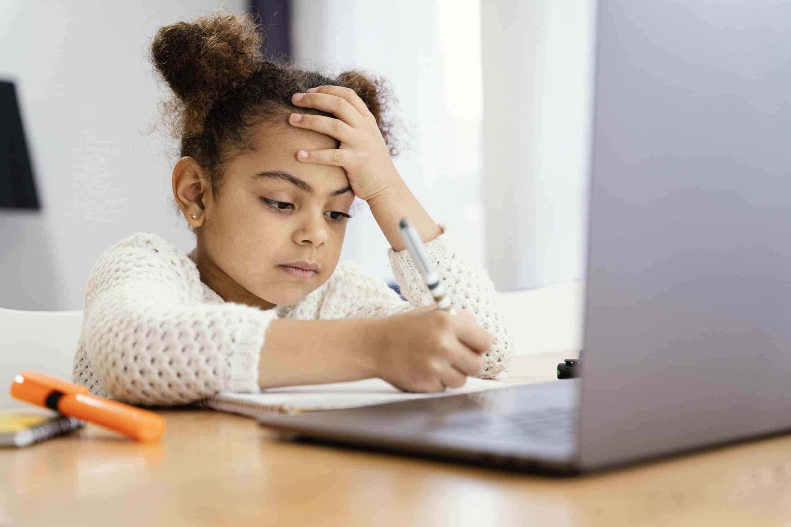 Menina estudando de frente para notebook, aparentando preocupação.